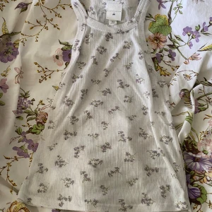 Blommig linne - Ett blommigt linne med lila blommor i storlek XS men passar även mig som har M då den är stretchig. Jätte bekväm men lite genomskinlig!