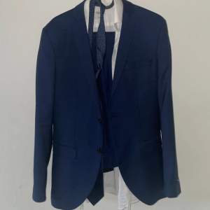 Mörkblå kostym (kavaj, vit skjorta, kostymbyxor och slips) endast använd en gång, som ny. Perfekt för skolbal. Storlek S (passar 160-175) 