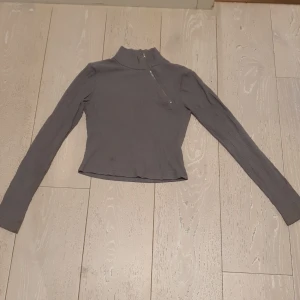 NA-KD En grå ribbad tröja med en dragkedja diagonalt ner till bröstet. - Storlek XS. 