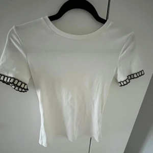 T-shirt med detalj i ärmen - Vit t-shirt med guld och svart detalj i ärmen. Använd några enstaka gånger.