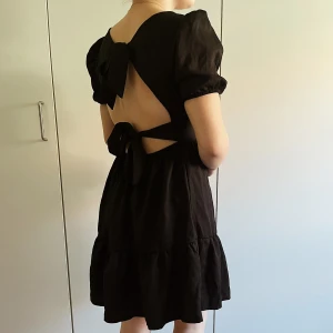 Svart Volangklänning - Denna klänning har ett rätt stramt material vilket gör att den sitter där den sitter vilket är bra. Charmen sitter i klänningens rygg och kan vara superfin till i sommar!