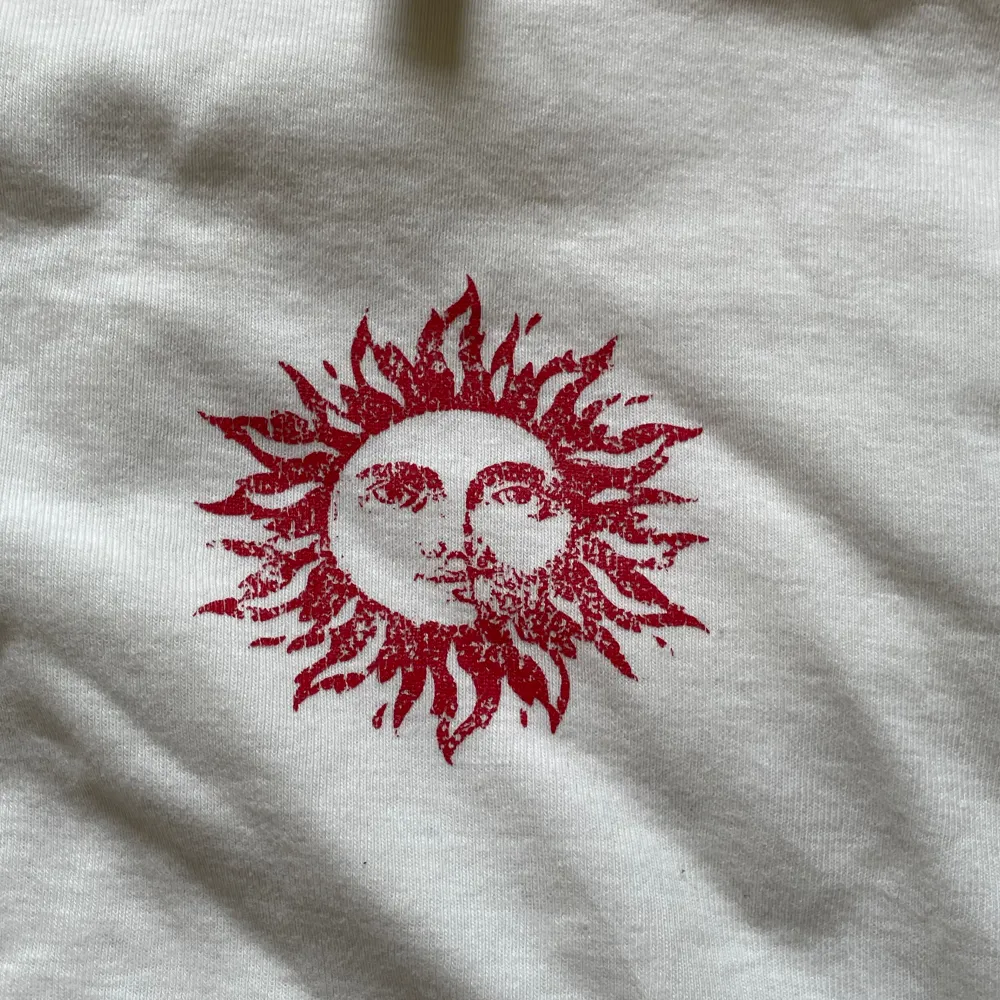 Vit croptop med tryck i mitten av en röd sol. Liten i storleken  Skick: använd. T-shirts.