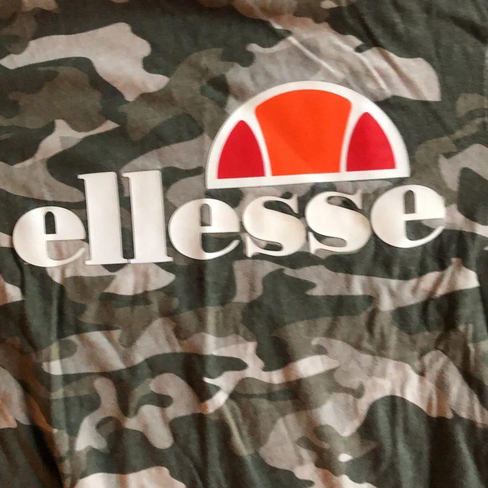 En kamouflagefärgad t-shirt från Ellesse med korta ärmar. T-shirten har ett stort tryck av Ellesse-logotypen på framsidan i vitt och orange. Tröjan har använts ett fåtal gånger men inte många gånger!. T-shirts.