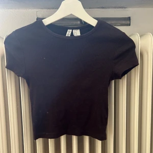 Svart ribbad topp från Gina Tricot - En svart ribbad topp från hm med korta ärmar. Toppen har en rund halsringning och är i en tight passform.