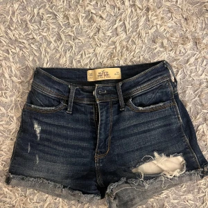 Mörkblåa jeansshorts - Säljer dessa mörk blåa jeansshorts med hål i från hollister. I storlek W23, men de är stretchiga i midjan så passar någon som har W25/26.