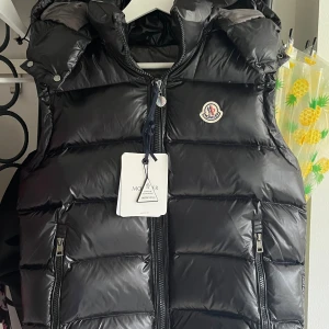 Moncler väst äkta  - Hej säljer nu min Moncler väst med luva (går att ta bort). Materialet är tjockt med mycket bra kvalitet, alla taggar och nfc scans fungerar som de ska. Påse och allt ni ser medföljer samt lappar. Skriv gärna om ni har några frågor eller funderingar😊🙏