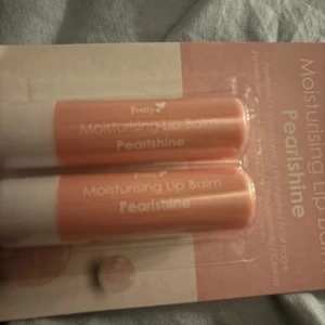 Moisturising Lip Balm Pearlshine - Ett paket med två fuktgivande läppbalsam från märket Pretty. Läppbalsamen har en pärlglans finish och kommer i en ljusrosa förpackning med vit botten.
