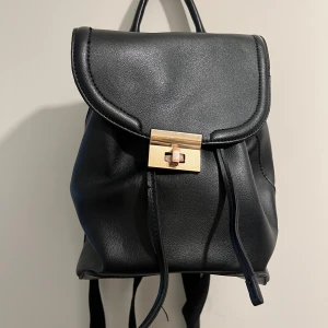 Ryggsäck TOPSHOP - Mindre ryggsäck från TOPSHOP, man kan se att den är använd på banden man drar i gen den med och på knappen (se bild två) 