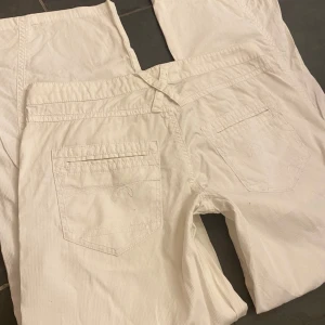 Vida byxor - Vida byxor av okänt material, men tunna och perfekta för sommaren. Vit/creméfärgade Midja: 40cm men med knytbara snören Innerbenlängden: 73cm, går att sprätta trådarna längst ned för att öka längden.