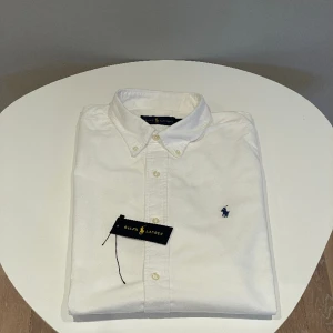 Ralph Lauren Skjorta  - Säljer min vita Ralph Lauren skjorta! Skjortan är i storlek L och modellen på bilden är ca 190cm och väger 80kg. Den är nästan helt ny och man ser inga tecken på att den är använd. Den klippta taggen finns och skickas med. Skriv för mer information!