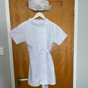 En sjuksköterske koatym, extremt kort, finns ett band man knyter med bakom ryggen men den är trasig. Hatt medföljer