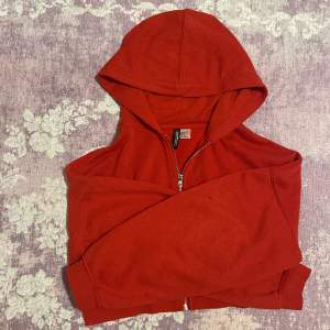 En kroppad hoodie i röd från H&M i storlek S. Är relativt använd men syns inte på plagget:)