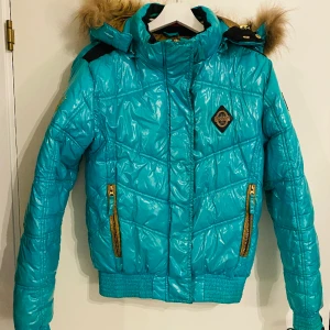Turkos glansig Nickelson jacka - Ovanlig Nickelson puffer jacka i glansigt material med avtagbar huva med fuskpäls. Mycket bra skick, skicka meddelande för mått.