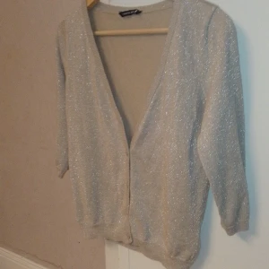 Guldglittrig kofta XS/S - Kofta som glittrar i guld och silver. Bra skick förutom att den översta knappen saknas vilket inte har stört mig då jag oftast haft den uppknäppt. Lätt att sy dit en ny om man har vilja och ork 😊 