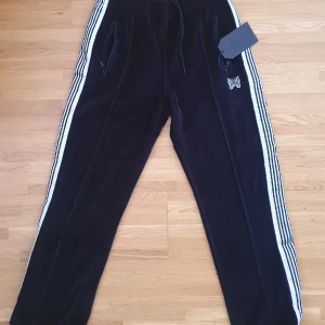 Needles Trackpants Helt nya!  - Helt nya Unisex Needles Trackpants i svart med silvriga stripes! Riktigt sköna i velvet material. Passar både killar och tjejer!   Storlek M passar 170-180cm beroende på eftertraktad passform. 