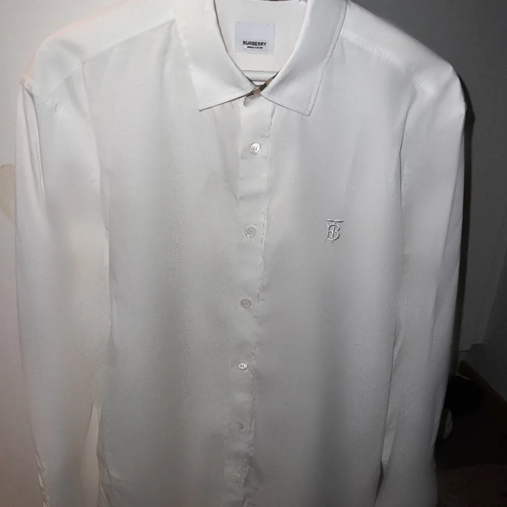 Storlek L, använd en gång. Tillverkad av 100% bomull, har denna skjorta en optisk vit rutig tryck, en klassisk krage och en knappknäppning framtill. De långa ärmarna med knappade manschetter och den böjda fållen ger en touch av sofistikering till den. Skjortor.