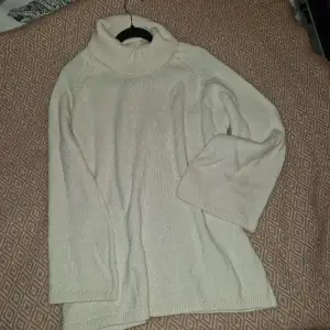 En vit stickad tröja från NA-KD, aldrig använd. Hög krage och stickade detaljer vid ärmar och nedtill på tröjan. Breda ärmar och lös passform.