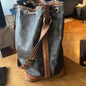 Äkta Louis vuttion Handbag NOÉ - En äkta ganska upptill sliten Louis vuttion väska i färgen leather Brown. Väskan är annars i väldigt fint vintage skick. Väskan är köpt vintage på Vestiaire Collective. Jag står inte för postens slarv.