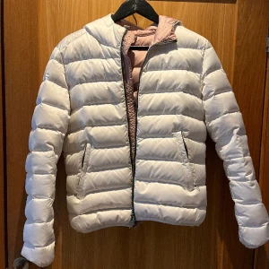 Colmar Jacka  - Säljer denna supersnygga colmar jackan som är vit på utsidan med en rosa insida.  Jackan stängs med en dragkedja och har en fast huva och elastiska ärmslut. Den är vattenavvisnde och är en tunnare dunjacka som är perfekt nu till våren!  O pris: 4999k