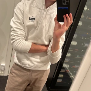 Vit Levi’s hoodie med tryck på ryggen - Inga tryck som har tappat färg, skön och trevlig att ha på sig och håller sig i väldigt bra kvalitet.