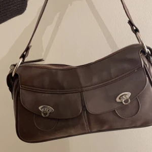 Brun handväska  - Medelstor handväska, köpt på second hand så vet ej vart den kommer ifrån. Bandet är lite nött men ingenting som syns. Hör gärna av dig för fler bilder, prisförslag mm.