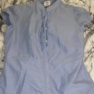 Blå spets t shirt - Är du förälskad i Stockholms stilen eller vill du bara ha en fin tröja inför sommaren? Ja då har du hittat rätt!! Detta är en fin blus man kan knäppa upp och passar till allt!