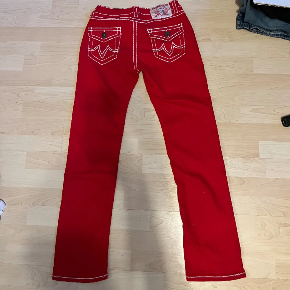 Röda True religon liknande byxor med vita sömar & detaljer längst med byxorna och på fickorna  Midjemått rakt över= 40cm Innerbenslängd= 75cm Längd på hela= 103cm . Jeans & Byxor.