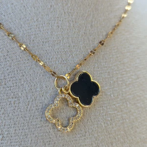 Guldhalsband med fyrklöverhänge - Ett elegant guldhalsband med ett fyrklöverformat hänge. Hänget har en svart insida och är dekorerat med små glittrande stenar runt om. Halsbandet har en fin, glittrande kedja som kompletterar hänget perfekt.aldrig använt 
