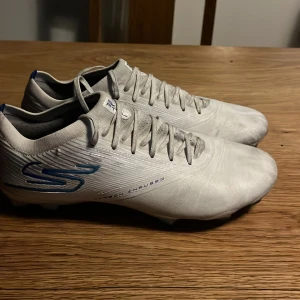 Sketchers razor Diamond ice vita  - Skicket är 7/10  Dom är använda cirka 2/3 veckor efter köp på konstgräs, där av det vita lite missfärgat. Inga problem med bobbar eller något annat slitage. Ny pris 2500kr köpta på unisport säljs på grund av ingen användning av dom. 