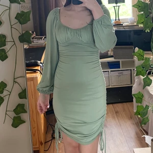 Grön klänning sommarklänning med fina detaljer smock puffärm knyt rosett Adoore liknande - En grön klänning med fina detaljer, liknar vissa modeller från Adoore! Har en svart prick på ena axeln som inte går bort. Lite ”luddig” i tyget jämfört med nyskick, men syns endast när man kollar riktigt nära.