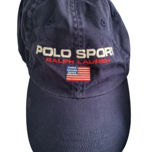 Ralph Lauren Polo sport keps - En keps ifrån Ralph Lauren polo sport. Kepsen är I väldigt bra skick och endast använd ett fåtal gånger.  Går att justera kepsen baktill så deb ska passa dem flesta.