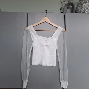 Vit spetstopp, spetsblus, blus med meshärm, smock, puffärm strl XS  - Vit spetstopp, spetsblus, blus med meshärm, smock, puffärm strl XS. Kan bäras med axlar uppe eller offschoulder. Använd en gång, mycket fint skick. Djurfritt och rökfritt hem. Missa inte mina andra annonser ❤️