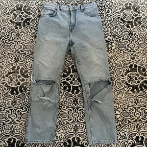 Ljusa jeans - Ljusa jeans med hål på knäna. Det högra hålet har blivit lite större än ursprungligen, men det är inget som förstör byxan. Annars är dem i fint skick. På mig som är 178 blir dem lite kortare i benen, slutar ovanför anklarna. Strl 30