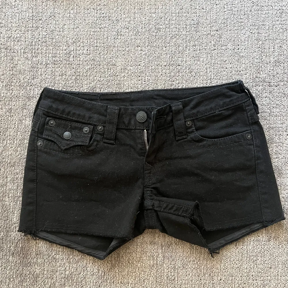 Midjemått är 36,5 cm raktöver och längden på shortsen är 30cm 🩷 Svarta jeansshorts från True Religion med klassisk femficksdesign och knappgylf. Shortsen har en rå kant vid bensluten och dekorativa sömmar på bakfickorna.. Shorts.