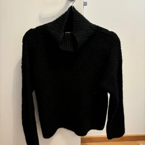 Svart stickad polotröja - En svart stickad polotröja med långa ärmar. Tröjan har en hög krage och är ribbstickad.
