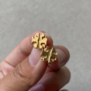 Tory Burch örhängen - Guldiga örhängen från Tory Burch 🌟 Supersnygga örhängen med varumärkets logga 🌟 Använda i fint skick, lite plättering som försvunnit på ena pluppen.  🌟 Ordpris 1099kr  
