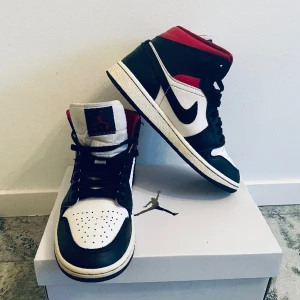 Jordan 1 Mid - Jordan 1 Mid i färgerna svart/vit/röd. Väldigt bra skick, inga skador men plösen är något smutsig. Modellen är ”woman” vilket innebär lite smalare passform. Inköpta hösten 2022 på Footlocker. Nypris ca 1400 kr. 