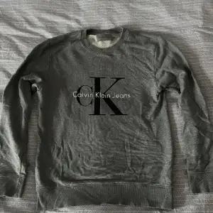 Grå Calvin Klein Sweatshirt med tryck på bröstet.  Nypris: 999kr  Skick: Mycket bra, sparsamt använd, utan synliga brister