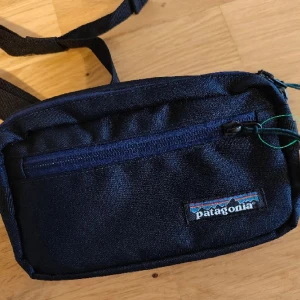 Helt NY Patagonia midjeväska blå - Helt ny och oanvänd! Fått denna i present men har redan en som jag använder. 3 fack. Mörk marinblå. För frågor eller fler bilder skriv PM! Köpare betalar frakt eller avhämtning, priset är fast.
