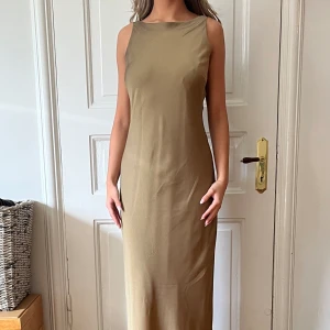 Långklänning  - A-line skuren lånklänning. Olivgrön med skirt yttre lager. Fin ryggringning med strassspännen, se bild. Använd två gånger. Om spännena tas loss kan klänningen handtvättas. 