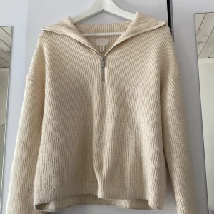 Stickad tröja  - Snygg basic cremevit tröja med halv zip up!! Använd så den har blivit lite nopprig, har även ett hål i sömmen vid ärmen som var från början. Köpt för 299kr säljer för 30kr