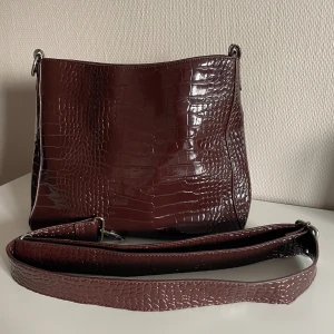 Brun axelremsväska - Brun axelremsväska som går att skystera i längd med rämmen. Väskan är i fint skick och sparsamt använd. Väskan är inköpt den Illums bolighus i Malmö. Väskan är köpt för 900kr. 