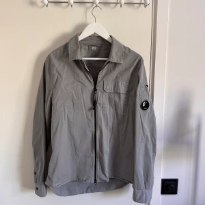 CP company overshirt - En grå CP company overshirt med dragkedja i storlek M.  Använd 2 gånger och därför säljs den. Väldigt tunn och perfekt för vår och sommar. 