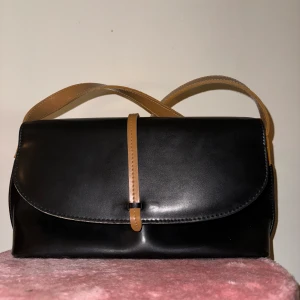 Axelremsväska  - Svart lite större axelremsväska med bruna detaljer. Sparsamt använd och inga tecken på användning. Mått ca 35x18.