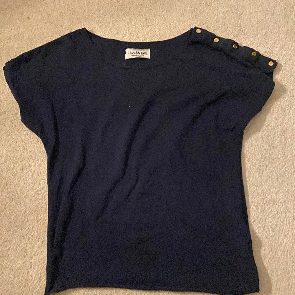 En mörkblå tröja från Jean Paul i storlek xs. Den har guldiga knappar på ena sidan av armen. Bara att skriva om ni har frågor. . T-shirts.
