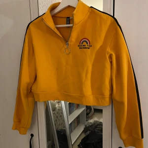 Senapsgul cropped turtleneck tröja - En cropped senapsgul turtleneck tröja med dragkedja upptill samt tryck av en regnbåge och en text under där det står ”chase the rainbow”!🌟 Från H&M i strl XS, knappt använd!💓