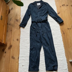 Blå overall - Blå overall/byxdress i jeanstyg med knytning i midjan. Knappt använd, nyskick! 