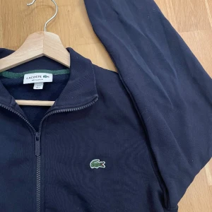 LACOSTE FULLZIP - Tjena säljer denna marinblå Lacoste fullzip tröjan. Tröjan är köpt från Zalando och har använts sparsamt.  Säljs då den inte kommer till användning längre. Kontakta gärna om det finns frågor👍