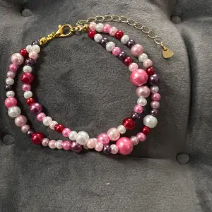 Egentillverkat armband med pärlor i två rader i olika rosa nyanser och guldigt spänne. Justerbar passform mellan 19-25 cm.