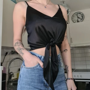 Svart topp - Svart glansig topp med knytning fram. Använd 1 gång, normal i storleken. Kom med prisförslag 😊  Material: 100% Polyester.